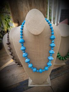 a necklace with blue glass beads on a mannequin head stand in front of a store display