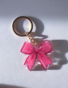 a pink bow shaped keychain sitting on top of a white table next to a shadow