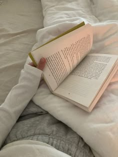 a person laying in bed reading a book with their hands on top of the book