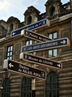 several street signs are posted in front of an old building with windows and balconies