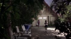 two women standing in front of a house with lawn chairs on the side walk way