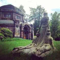 an old building with a statue in front of it on the grass near a tree stump