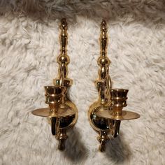 two brass candle holders on a white carpet with one light turned on and the other turned off