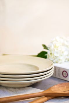 a stack of white plates sitting on top of a table next to wooden spoons