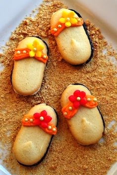 four decorated cookies sitting in the sand on top of a white plate with red, yellow and orange bows