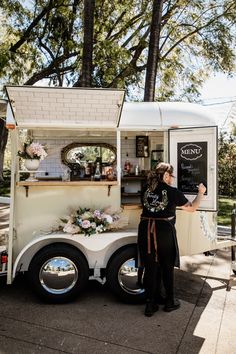 a woman standing in front of a food truck with a chalkboard sign on it