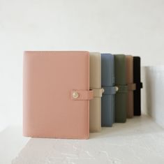 four different colored notebooks lined up on a white surface with one open and the other closed