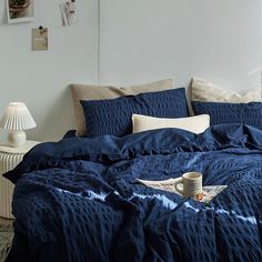 a bed with blue comforter and pillows in a white room next to a lamp