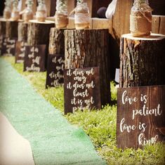 wooden signs are lined up on the grass near some logs with flowers in jars and saying love is patient love is kind