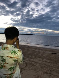 a man standing on top of a sandy beach next to the ocean talking on a cell phone