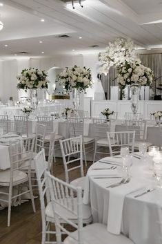 a room filled with lots of white tables covered in white cloths and centerpieces