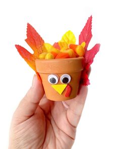 a hand holding a clay pot filled with candy corn and a fake turkey in it