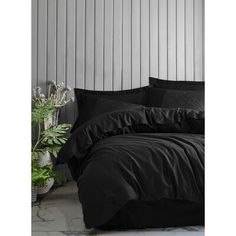 a bed with black sheets and pillows next to a potted plant