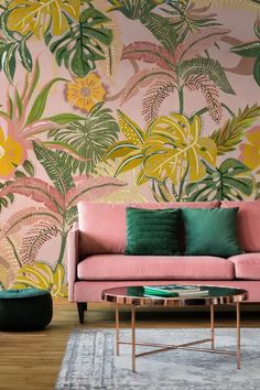 a pink couch sitting in front of a wall with green and yellow flowers on it