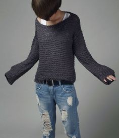 a woman in ripped jeans and a sweater with her arms spread out, standing against a gray background