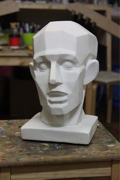 a white sculpture of a man's head sitting on top of a wooden table