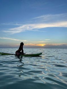 a woman sitting on top of a surfboard in the middle of the ocean at sunset