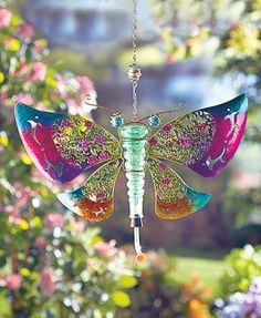 a colorful glass dragon wind catcher hanging from a tree in front of some pink flowers