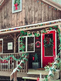 the front porch of a cabin decorated for christmas with wreaths and lights on it