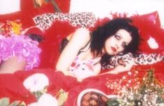 a woman laying on top of a red bed covered in pillows and blankets next to flowers