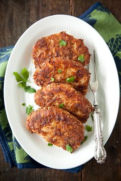 three crab cakes on a white plate with a fork and napkin next to it, ready to be eaten