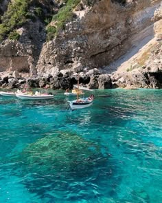 two small boats floating on top of a blue body of water next to a rocky cliff