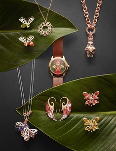 the watches and necklaces are on display in front of green leaves, with butterfly pendants