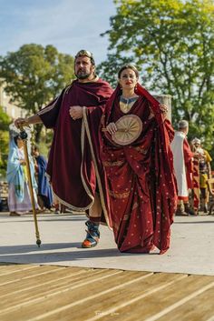 a man and woman dressed in medieval clothing walking down the street with their arms around each other