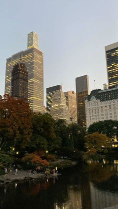 the city skyline is lit up at night, with people walking around in the park