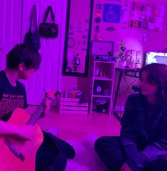 two people sitting on the floor playing guitar in a room with purple lights and pink lighting