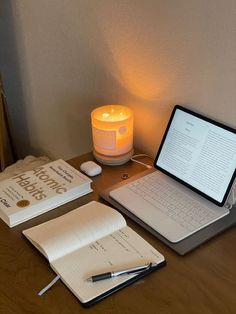 an open laptop computer sitting on top of a wooden desk next to a notebook and candle