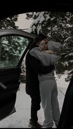 two people standing next to each other in front of a car with snow on the ground