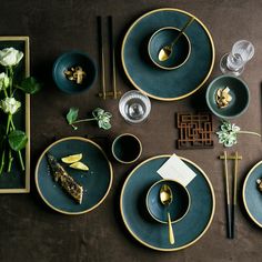 the table is set with blue plates and silverware, gold utensils and flowers