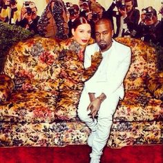 a man and woman sitting on top of a couch in front of people taking pictures