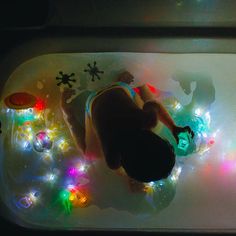 a person laying in a bath tub with christmas lights on the floor next to it