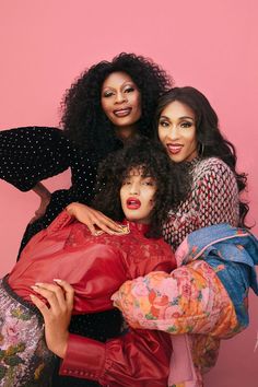 three women posing for the camera in front of a pink background