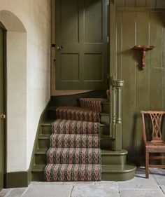 a green door and some stairs in a room with a chair on the floor next to it