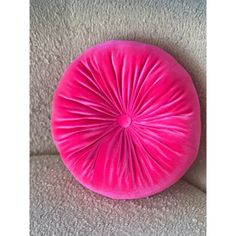 a pink round pillow sitting on top of a white carpeted floor next to a wall