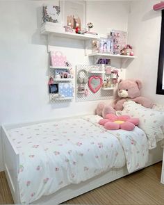 a teddy bear sitting on top of a bed in a room with shelves above it