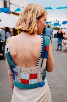 a woman walking down the street with an open back sweater over her shoulders and people in the background