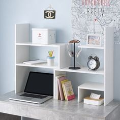 a laptop computer sitting on top of a white book shelf next to a wall mounted clock