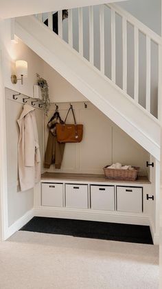 an entryway with white storage drawers under the stair case and coat rack underneath it