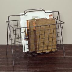 a wire basket with books and magazines in it on a wooden table next to a white wall