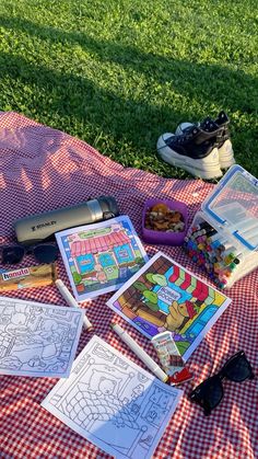 a picnic blanket with coloring books and other items on it in the grass next to a pair of shoes