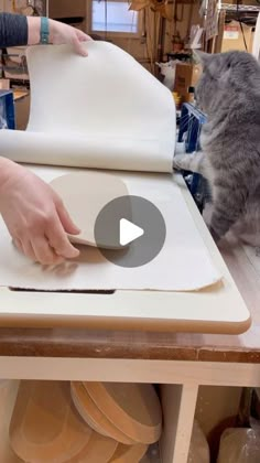 a woman is cutting up some plates on a table with a cat looking at her