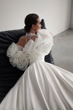 a woman in a white dress sitting on a black chair with her back to the camera