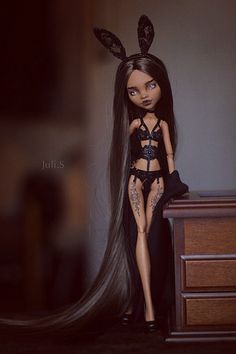 a doll with long hair sitting on top of a table next to a dresser and bed