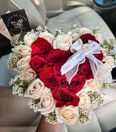 a heart shaped arrangement with roses and baby's breath ribbon in someones lap