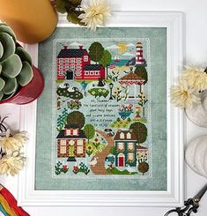 a cross stitch pattern with houses and trees on it, surrounded by other crafting supplies