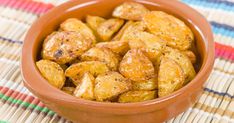 a brown bowl filled with fried potatoes on top of a colorful table cloth next to a wooden spoon